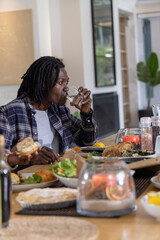 Naklejka premium African American friends sitting at dining table at home drinking from glasses and sharing chicken
