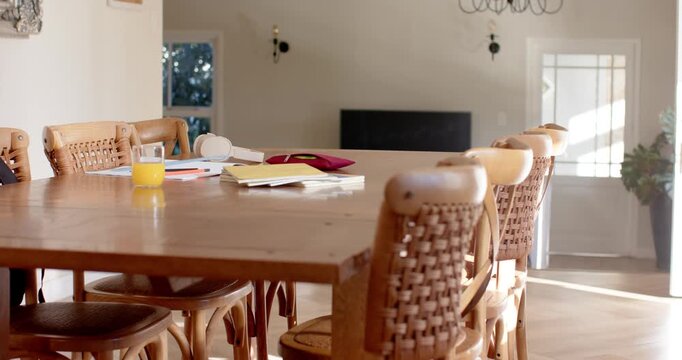 Camera is slowly moving forward and right across wooden table, revealing chair weave and notebooks