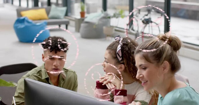 Coworkers leaning by monitor showing animated pink rings growing over faces, guiding design review