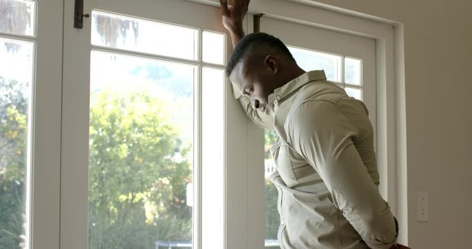 African American man pausing by glass door frame, leaning and lowering head, reflecting, copy space