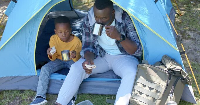 African American father and son taking snack break at blue tent, man checking metal pot