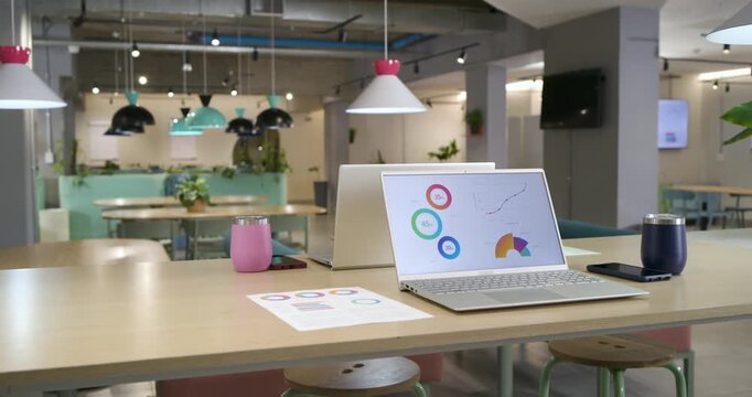 Slider camera is sliding forward-right and zooming on silver laptop on wooden table showing charts