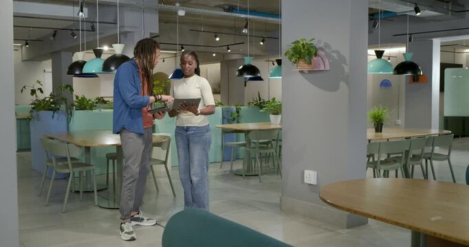 Coworkers noticing update on tablet, in break area collaborating on tablets, pointing and smiling