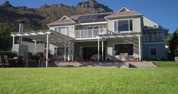 Sun is moving, two-story house and pergola are casting shifting shadows across deck and lawn