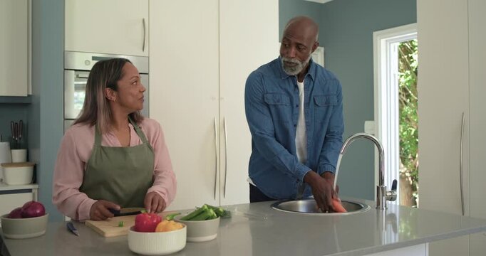 Diverse couple starting cooking, chopping green onions on cutting board and washing carrots at sink