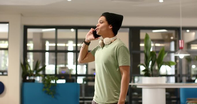 African American man raising smartphone to right ear, speaking and gesturing in modern lobby