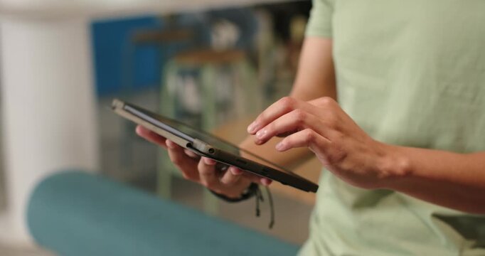 Adult male is tapping and swiping tablet in casual lounge after adjusting grip to browse content