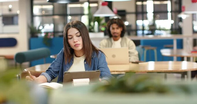 African American classmates studying in coworking space, woman taking notes from tablet for exam