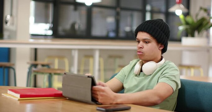 African American man sitting in study lounge tilting tablet, reacting to tablet, smirking