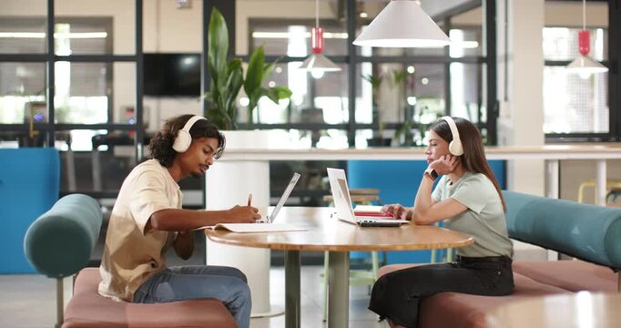 African American students studying assignment in study room flipping notebook and typing on laptops