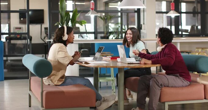 African classmates arriving and greeting, settling at round table in study lounge, sharing laptops