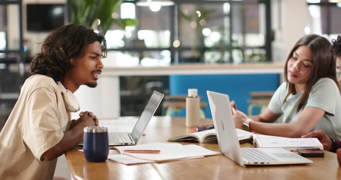 African American students studying at table while right man showing striped folder with laptops