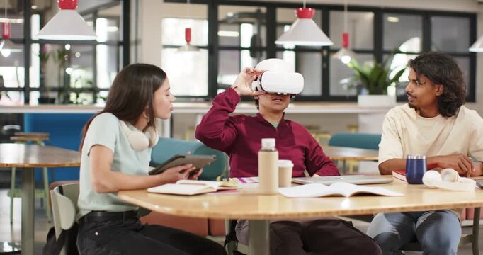 Diverse students watching center male reaching for VR headset, testing for project in study lounge