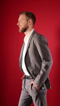 Fashion model. Handsome man in stylish outfit walking on red background