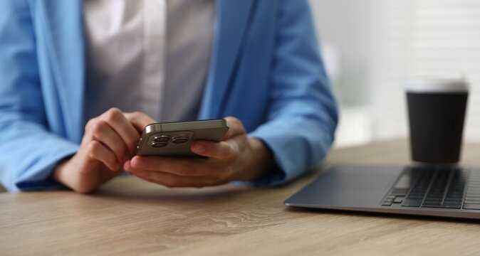 Woman sending text message via smartphone at wooden desk indoors, closeup
