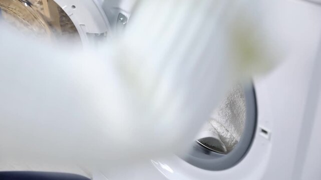 Woman putting towels into washing machine and taking bottle of detergent at home, closeup