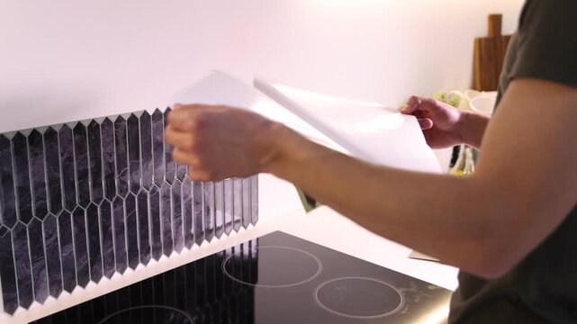 Man applying peel and stick tiles onto wall in kitchen, closeup. Camera moving forward