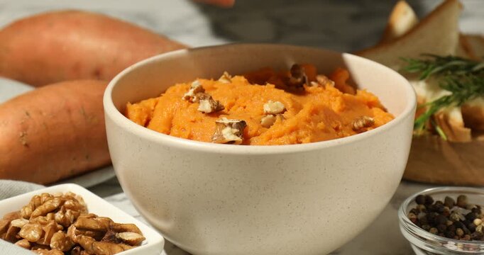 Woman adding walnuts and rosemary onto mashed sweet potato at table, closeup
