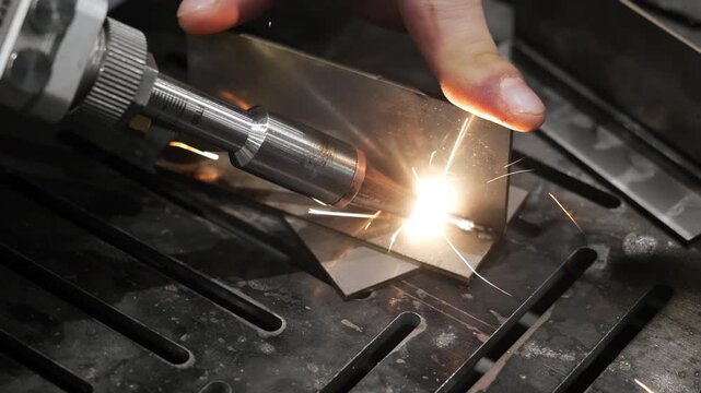 Laser welding metal parts with precision welding tool producing bright sparks during industrial metal fabrication process in manufacturing workshop.