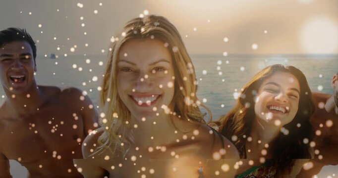 Leaning center woman in blue strapless bikini posing for camera smiling at beach as sun sparkles