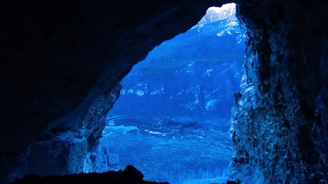 View from inside a dark cave entrance out to a mountain canyon as the light increases, time lapse