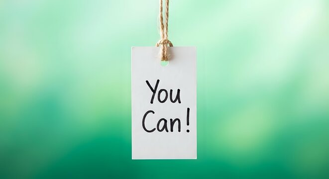 Motivational white paper tag with You Can text hanging on rope against soft green bokeh background for encouragement and positive mindset concepts.