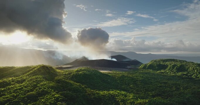 Mount Yasur volcano on Tanna Island in Vanuatu actively erupting, releasing smoke and ash in cloudy sky above lush green landscape, sun rays breaking through dramatic clouds. Aerial view landscape