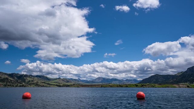 Big white clouds drifting over a mountain reservoir with red buoys floating on the water, Montana, time lapse