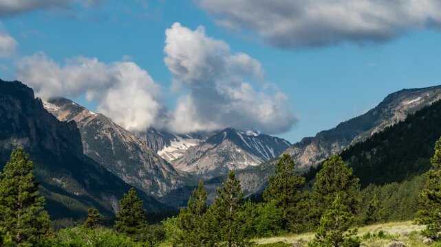 Cumulus clouds forming over snowy mountain peaks above a pine forest and meadow, Beartooth Mountains, Montana, time lapse