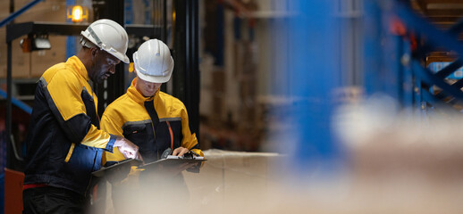 Two warehouse workers wearing safety helmets reviewing inventory checklist and logistics data in distribution center. Employees inspecting cargo and managing operations. © eakgrungenerd