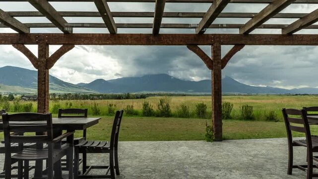 Storm clouds moving over mountains and a green meadow seen from a covered patio with tables and chairs, Paradise Valley, Montana, time lapse