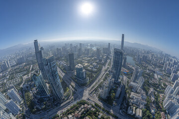 Fototapeta premium Aerial panorama of modern city with tall skyscraper buildings, wide road network, and clear blue sky under bright sunlight, showcasing urban architecture and cityscape