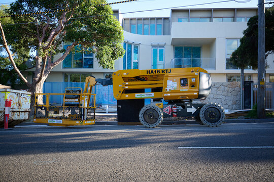 Side view of yellow Haulotte HA16 RTJ articulating boom parked and collapsed outside an under construction apartment building