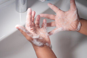Child Hands are covered in soap while washing at a sink with running water