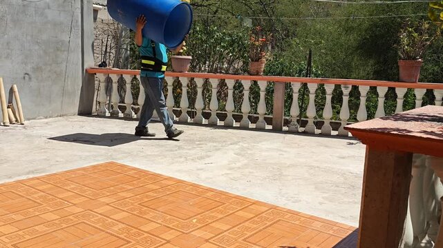 Man moving a blue water barrel on a house terrace