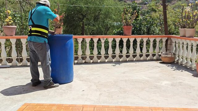 Person cleaning a large blue plastic barrel with a broom