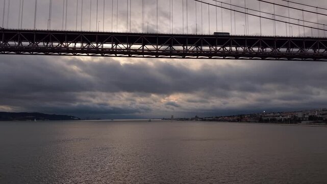 Silhouette of Ponte 25 de Abril road and rail bridge over Tagus river under an overcast sky, Lisbon