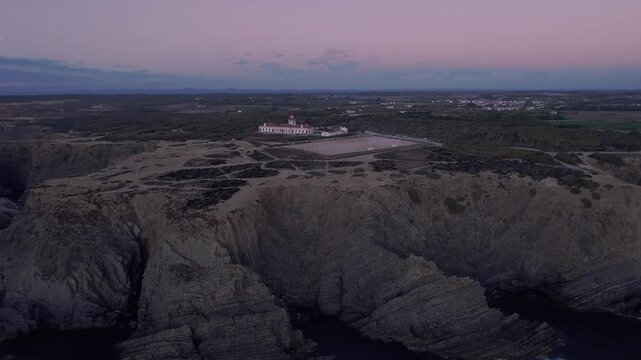 Historic Farol do Cabo Sard&atilde;o lighthouse overlooking stratified Atlantic cliffs within Parque Natural do Sudoeste Alentejano e Costa Vicentina, drone establishing shot.