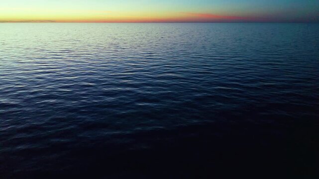 Calm ocean surface extends to the horizon at dusk with soft wave patterns and a warm gradient sky, creating a serene and tranquil seascape atmosphere.