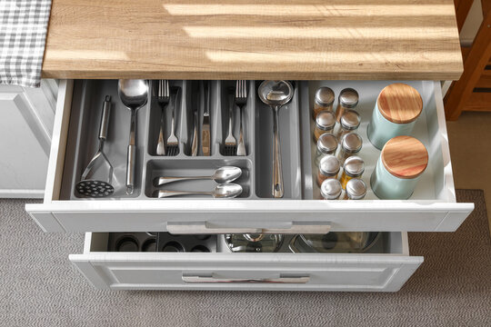 Open kitchen drawer with different silver cutlery and set of spices, top view