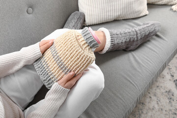 Fototapeta premium Young woman with hot water bottle sitting on sofa at home, top view