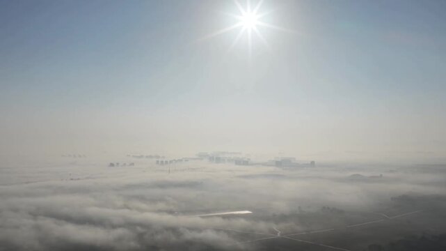 A static aerial timelapse showing modern skyscrapers emerging from a dense sea of clouds and advection fog under a brilliant sun in a coastal city in China.