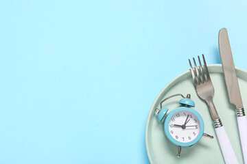 Table setting with alarm clock on blue background. Intermittent fasting concept