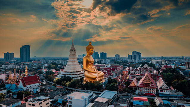Spectacular aerial view of the giant golden Buddha statue and stupa at Wat Paknam Bhasicharoen with dramatic sky and sunbeams in Bangkok, Thailand.