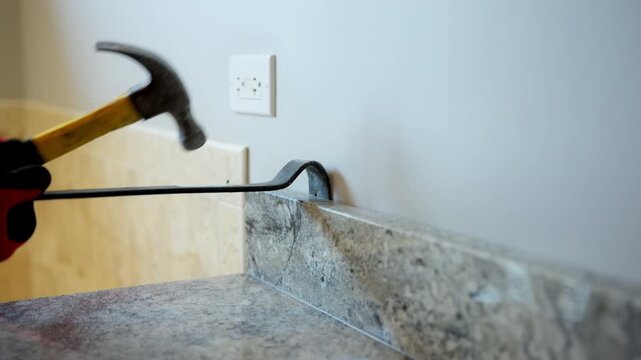 Worker removing old kitchen or bathroom furniture during home renovation using crowbar and hammer.