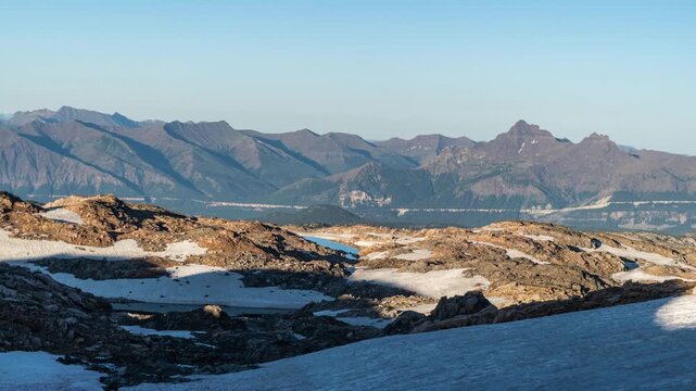 Morning sunlight growing across a rocky alpine plateau and snowfield with a mountain range beyond, Beartooth Plateau, Montana, time lapse