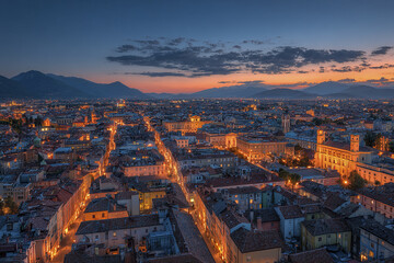 Obraz premium Wide city panorama of European old town at twilight with historic buildings and glowing street lights under colorful sky creating peaceful and charming atmosphere