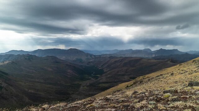 Dark storm clouds moving over deep forested valleys and ridges below a grassy slope, Absaroka Range, Montana, time lapse