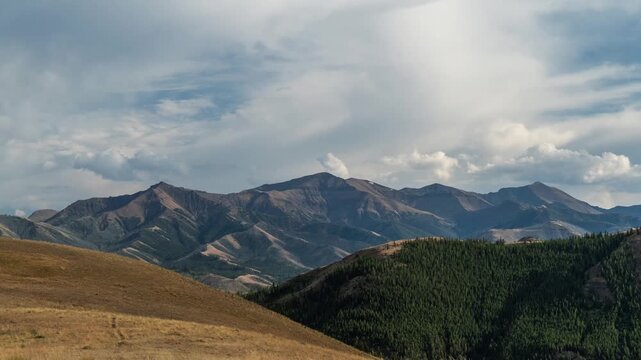 Clouds moving over rugged mountains above a golden grassy hillside and dark forest, Absaroka Range, Montana, time lapse