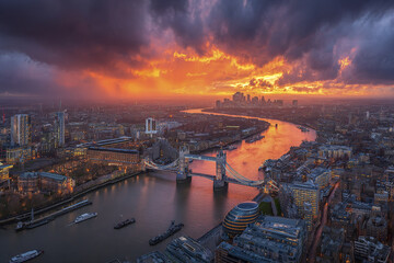 Obraz premium Sunset over city skyline with river winding through, featuring historic suspension bridge and modern buildings under dramatic clouds, creating vibrant and intense atmosphere